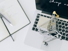 Miniatűr bevásárlókosár egy laptop billentyűzetén, a képernyőn a „Vásárolj most” felirattal