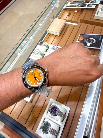 A csuklón viselt, tigris ihlette Seiko Prospex HBB005K1 búváróra, amelynek borostyánszínű, texturált számlapja, narancssárga díszítésű fekete kerete, valamint rozsdamentes acél tokja és karkötője látható.