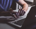 Gyenge fényben egy MacBook billentyűzetén gépelő kezek, az Apple logó ragyog