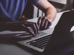 Gyenge fényben egy MacBook billentyűzetén gépelő kezek, az Apple logó ragyog
