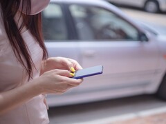 Egy nő az okostelefonján gépel, a háttérben egy ezüstszínű autóval