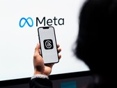Egy kéz egy okostelefont tart egy nagy Meta-logó előtt