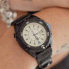 A Timex Intrepid x Dimepiece Blackout Edition fekete rozsdamentes acél tokkal, krémszínű számlappal és lila részletekkel rendelkezik
