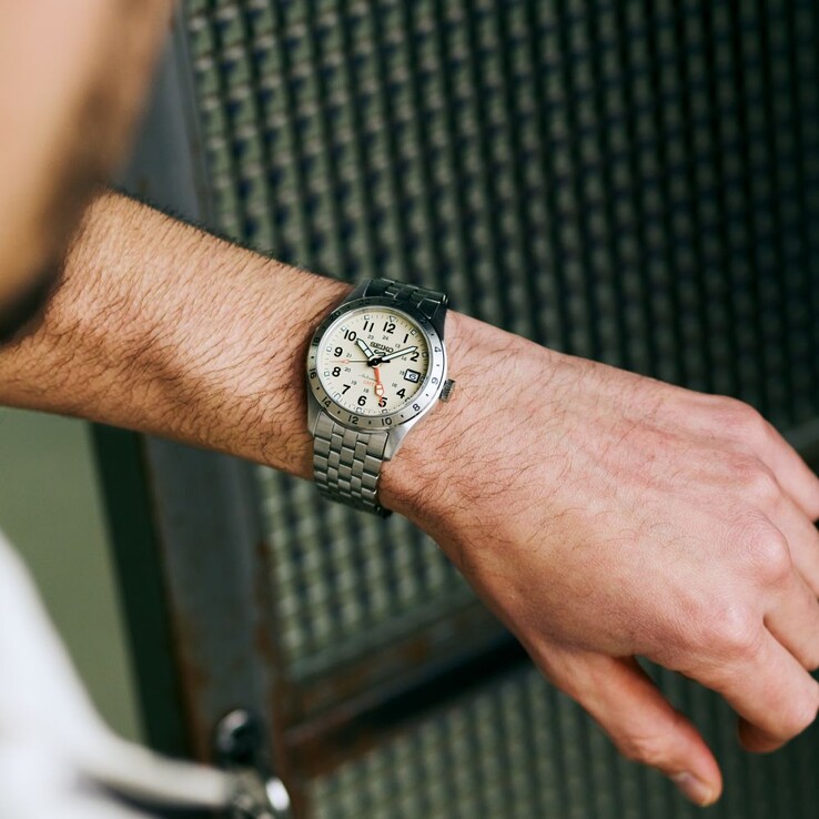A Seiko 5 Sports Field GMT HDB002 modell elölnézete: krém színű számlappal, narancssárga GMT-mutatóval, rögzített 24 órás kerettel és rozsdamentes acél karkötővel.