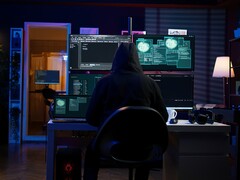 Egy csuklyás kutató több képernyőn dolgozik egy sötétített berendezésben. Általános hacker a képen.
