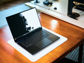 Egy nyitott, matt fekete Razer Blade 16 gamer laptop, amely egy fehér asztali szőnyegen fekszik egy meleg hangulatú faasztalon, élénk fekete-fehér háttérképpel.