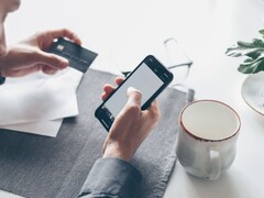 Egy személy, aki okostelefonját pötyögeti, miközben a másik kezében bankkártyát tart