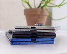 A közelgő Apple iPhone Fold koncepcióját reprezentáló összecsukható okostelefonok halmaza egy fehér asztalra helyezve, háttérben egy cserepes növénnyel (Kép forrása: Notebookcheck)