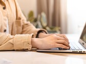 Egy világos íróasztalnál nyitott laptop billentyűzetén gépelő kezek
