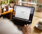 Egy személy laptop előtt, amelyen a Google kezdőlapja látható, egy csésze kávé mellett