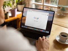 Egy személy laptop előtt, amelyen a Google kezdőlapja látható, egy csésze kávé mellett