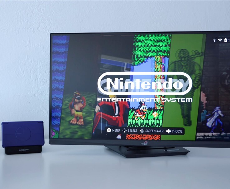 Retroid Pocket Flip 2 lila színben egy monitor melletti dokkolóra helyezve, a TV képernyőjén egy retro NES emulátor felület látható. (Kép forrása: Retro Game Corps a YouTube-on)