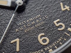 A Timex Expedition Field Post Titanium texturált fekete számlapjának közelképe arab számokkal, világító mutatókkal és jelölésekkel, valamint dátumablakkal.