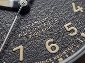 A Timex Expedition Field Post Titanium texturált fekete számlapjának közelképe arab számokkal, világító mutatókkal és jelölésekkel, valamint dátumablakkal.