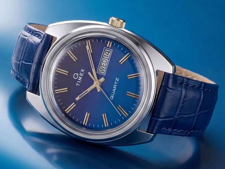 A Timex Q 1976 Day and Date ferde szögből készült termékfotója, amely kiemeli a kék színátmenetes számlapot, a polírozott rozsdamentes acél tokot és az aranyszínű koronát.