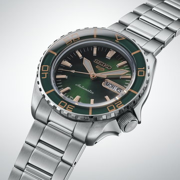 Közeli kép a Seiko 5 Sports SKX HDB005 óráról, amely kiemeli sötétzöld számlapját, rozéarany színű mutatóit és applikált indexeit, valamint a hozzá illő zöld lünettát aranyszínű jelölésekkel.