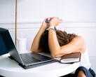 Egy nő, aki a laptopja mellett ülve a okostelefonjára néz