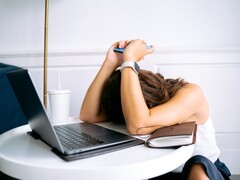 Egy nő, aki a laptopja mellett ülve a okostelefonjára néz