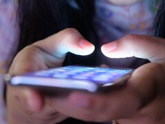 Két kéz tart egy világító képernyőjű okostelefont a félhomályban