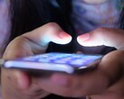Két kéz tart egy világító képernyőjű okostelefont a félhomályban