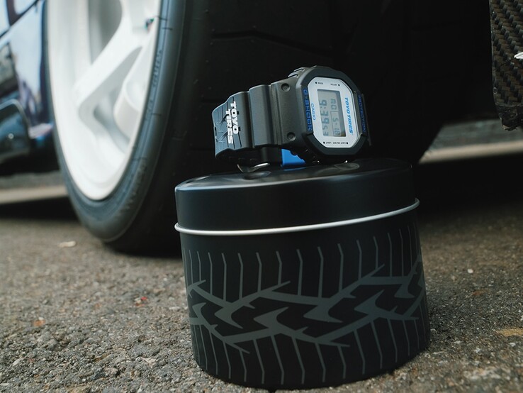 Casio G-Shock DW5600TT25-1 x Toyo Tires karóra, amelyet egy gumiabroncsot ábrázoló fémdobozban, egy autókerék mellett állítanak ki.
