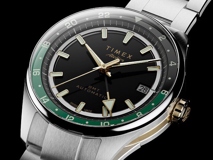 A Timex Atelier GMT Première M1a ferde nézete, amelyen látható a fekete számlap, a zöld GMT-gyűrű, az aranyszínű korona és a rozsdamentes acél szíj.