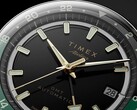 Közelkép a Timex Atelier GMT Première M1a fekete számlapjáról, aranyszínű mutatókkal, világító órajelölésekkel, dátumablakkal és fekete-zöld, 24 órás GMT-gyűrűvel.