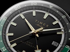 Közelkép a Timex Atelier GMT Première M1a fekete számlapjáról, aranyszínű mutatókkal, világító órajelölésekkel, dátumablakkal és fekete-zöld, 24 órás GMT-gyűrűvel.
