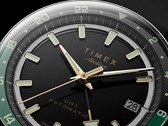 Közelkép a Timex Atelier GMT Première M1a fekete számlapjáról, aranyszínű mutatókkal, világító órajelölésekkel, dátumablakkal és fekete-zöld, 24 órás GMT-gyűrűvel.