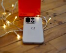 Egy OnePlus 15 fekszik egy faasztalon, meleg hangulatú fényfüzérekkel körülvéve, a háttérben pedig egy élénkpiros OnePlus doboz látható.