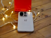 Egy OnePlus 15 fekszik egy faasztalon, meleg hangulatú fényfüzérekkel körülvéve, a háttérben pedig egy élénkpiros OnePlus doboz látható.