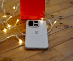 Egy OnePlus 15 fekszik egy faasztalon, meleg hangulatú fényfüzérekkel körülvéve, a háttérben pedig egy élénkpiros OnePlus doboz látható.
