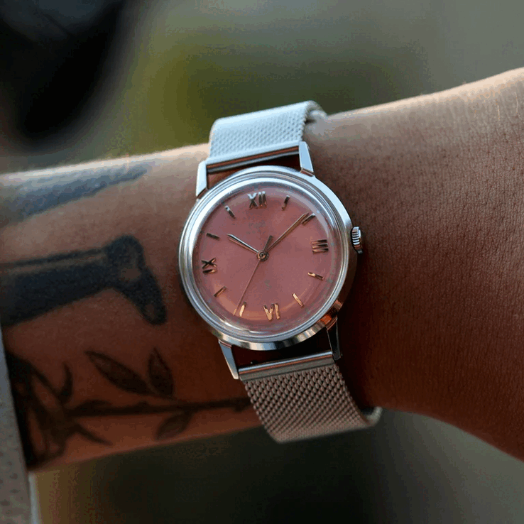 Egy személy, aki a Timex x Todd Snyder Marlin Mesh órát viseli, lazacszínű, napraforgós számlappal és hálós karkötővel.