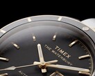 Közelkép a fekete számlapos Timex Waterbury Heritage Automatic óráról, amelyen láthatók a csiszolt, fényes mutatók, az órajelölők, a nap-dátum kijelző és a fekete keret.