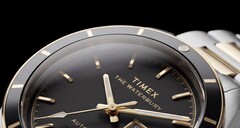 Közelkép a fekete számlapos Timex Waterbury Heritage Automatic óráról, amelyen láthatók a csiszolt, fényes mutatók, az órajelölők, a nap-dátum kijelző és a fekete keret.