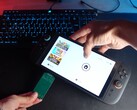 Yu a Better Gaming YouTube-csatornáról, egyik kezében egy Nintendo Switch 2, a másikban pedig egy nyílt forráskódú zöld PCB-adaptert tart, és megpróbálja behelyezni a készülék microSD Express foglalatába (Kép forrása: Better Gaming via YouTube)