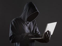 Egy csuklyás hacker egy laptopot kezel sötét háttér előtt.