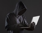 Egy csuklyás hacker egy laptopot kezel sötét háttér előtt.