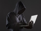 Egy csuklyás hacker egy laptopot kezel sötét háttér előtt.