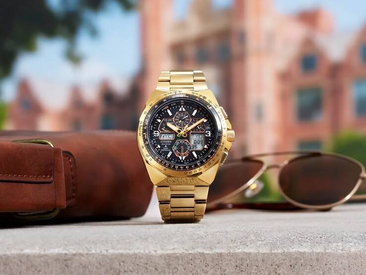 A Citizen Promaster Skyhawk A-T JY8144-50E arany színű pilótaóra egy párkányon áll, egy barna bőr táska és napszemüveg mellett, háttérben egy elmosódott városi tájjal.