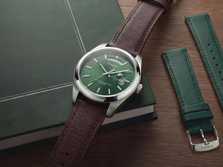 A zöld számlapos, barna bőrszíjas Timex Legacy Day and Date egy sötétzöld könyvön, a cserélhető zöld bőrszíj mellett.