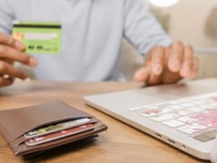 Egy személy bankkártyát tart egy laptop előtt, az íróasztalon egy pénztárca látható