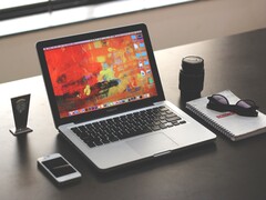 MacBook Pro egy sötét íróasztalon, okostelefon, szemüveg és jegyzetfüzet mellett