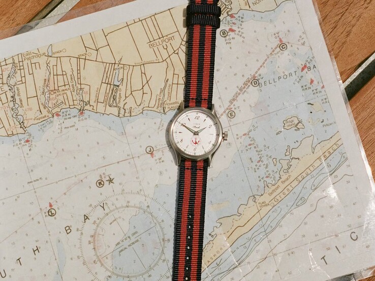 Noah x Timex MK1 Anchor karóra, sötétkék-piros csíkos szövet szíjjal, egy tengeri térképen fekve.
