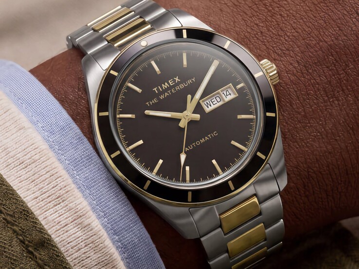 Két színű Timex Waterbury Heritage Automatic karóra fekete számlappal, csuklón viselve, látható a nap-dátum kijelzője és az arany színű díszítések.