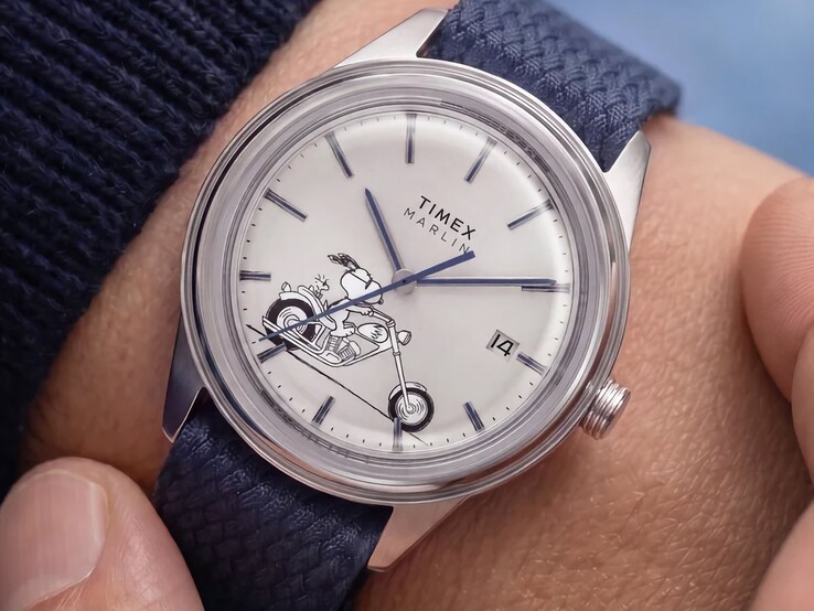 A csuklón viselt Peanuts x Timex Marlin Jet Automatic Easy Rider óra, amelynek ezüstfehér számlapján Snoopy motorkerékpáron ül, kék indexekkel és mutatókkal, valamint kék szövött szíjjal.