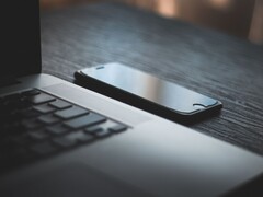 Egy okostelefon, amely egy sötét íróasztalon egy kinyitott laptop mellett fekszik
