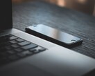Egy okostelefon, amely egy sötét íróasztalon egy kinyitott laptop mellett fekszik