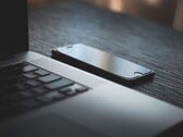 Egy okostelefon, amely egy sötét íróasztalon egy kinyitott laptop mellett fekszik