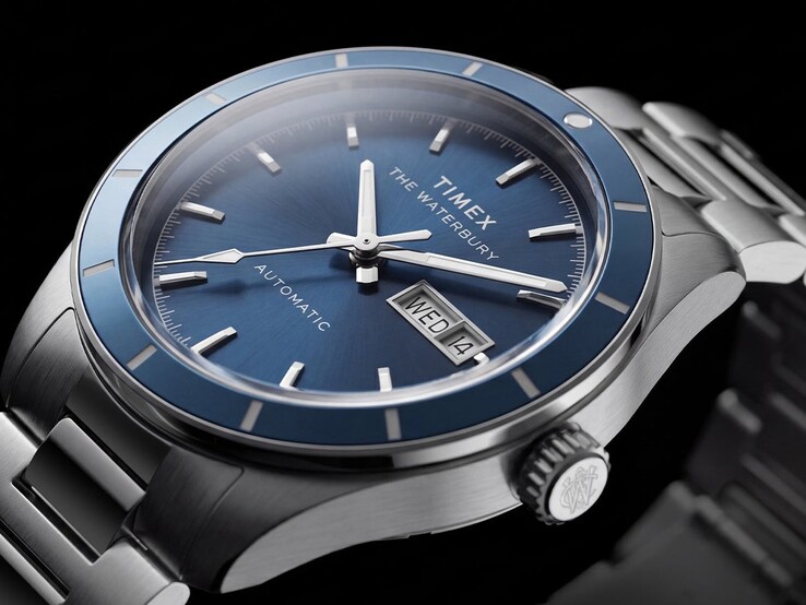 Közelkép a kék számlapos Timex Waterbury Heritage Automatic óráról, amelyen láthatók a világító mutatók, a felragasztott órajelölők, valamint a nap-dátum kijelző.